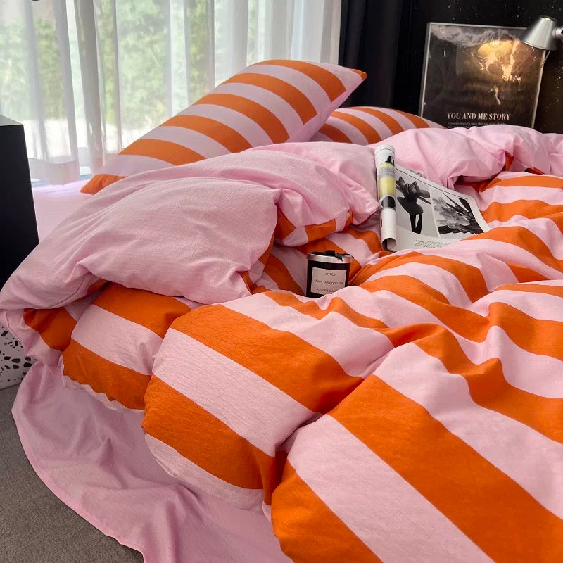 Pink and orange striped bedding set on a bed, featuring a duvet cover and matching pillowcases in a styled bedroom setting.