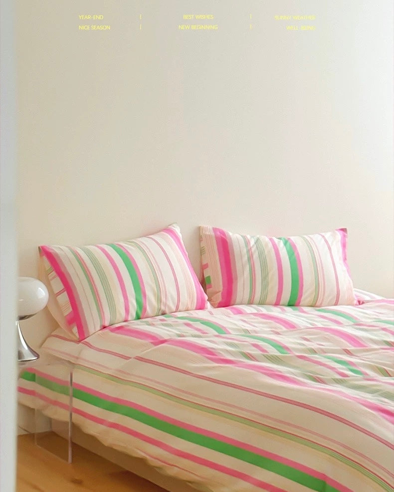 Striped pink and green bedding on a bed with a white wall in the background