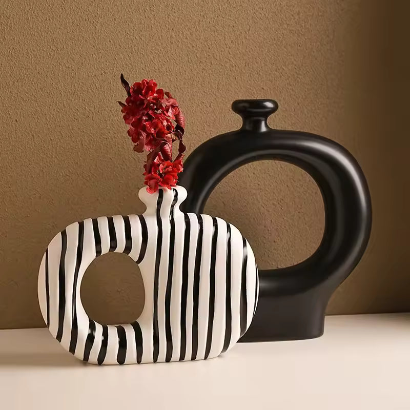 Black and white striped vase with red flowers next to a black vase on a beige surface.