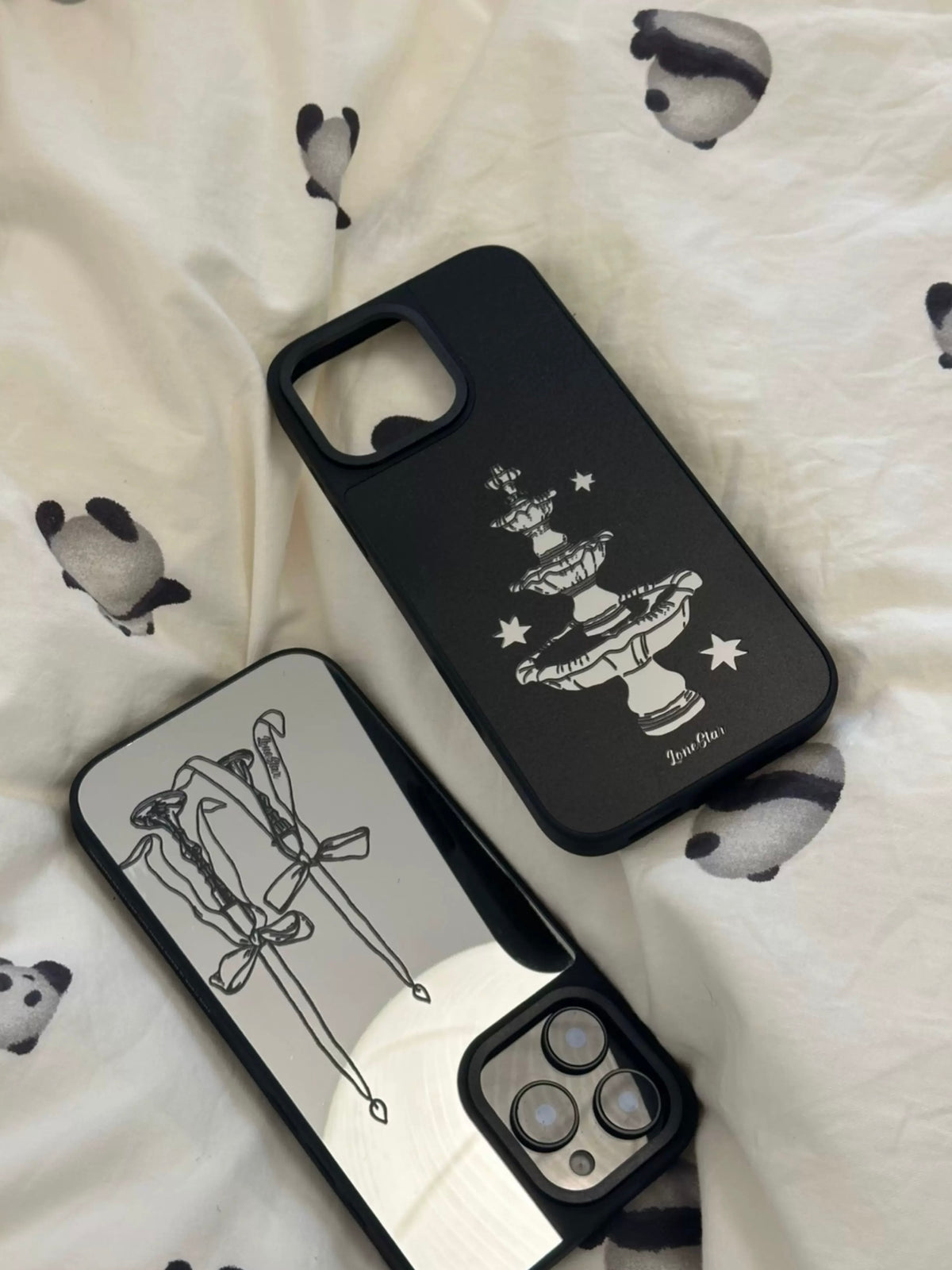 A Coquette phone case with bow candles lies diagonally beside the black fountain version.