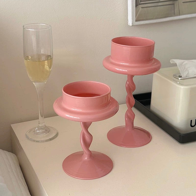 Two pink candle holders on a surface with a glass of white wine in the background.