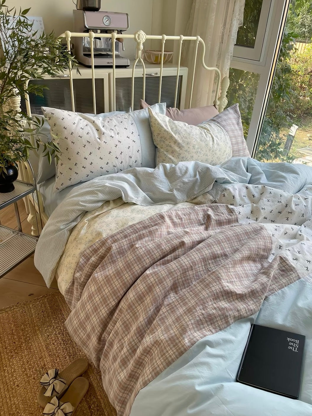 Blue and brown patchwork bedding spread across a cream metal bed beside a large window.