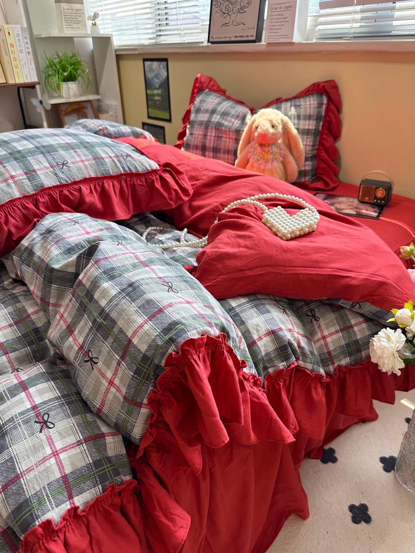 Plaid bedding with red ruffles on a bed in a room with a teddy bear and decorative items.