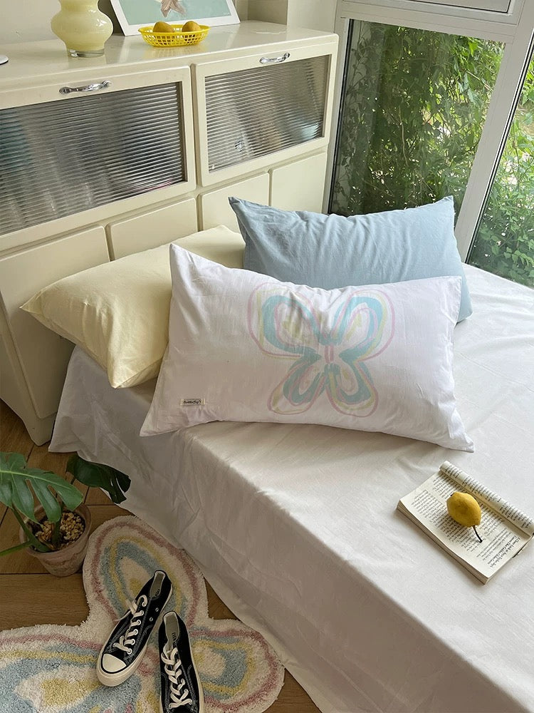 Pastel butterfly pillowcase arranged on a white bed beside pale blue and yellow pillows.