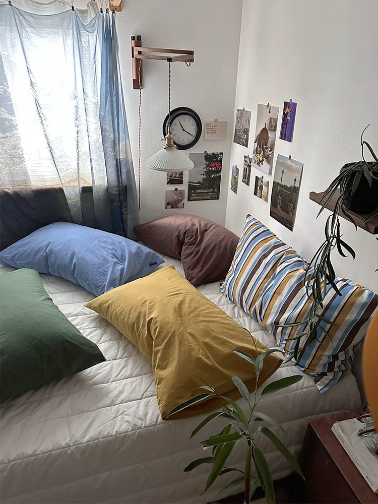 A Preppy pillowcase with colorful stripes sits in front of solid mustard, blue and mocha pillowcases.