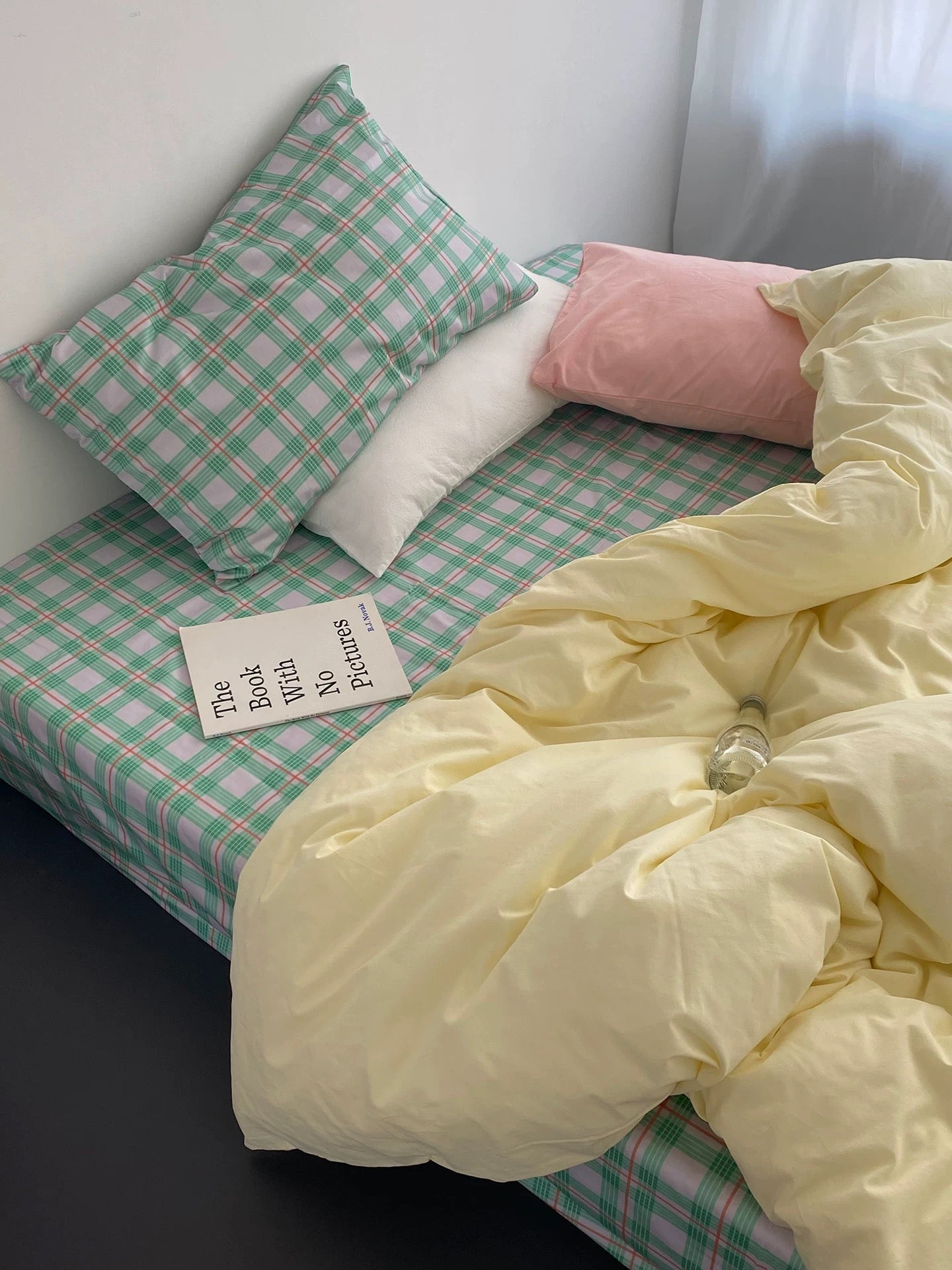 Bed with checkered green and white sheets, yellow comforter, and pink pillow.