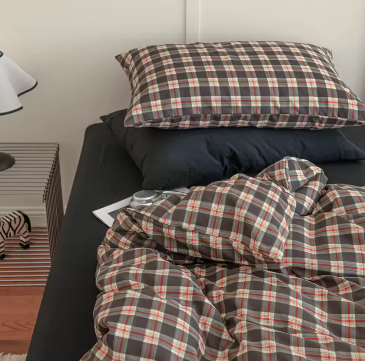 Plaid bedding set on a bed with a side table and lamp in the background