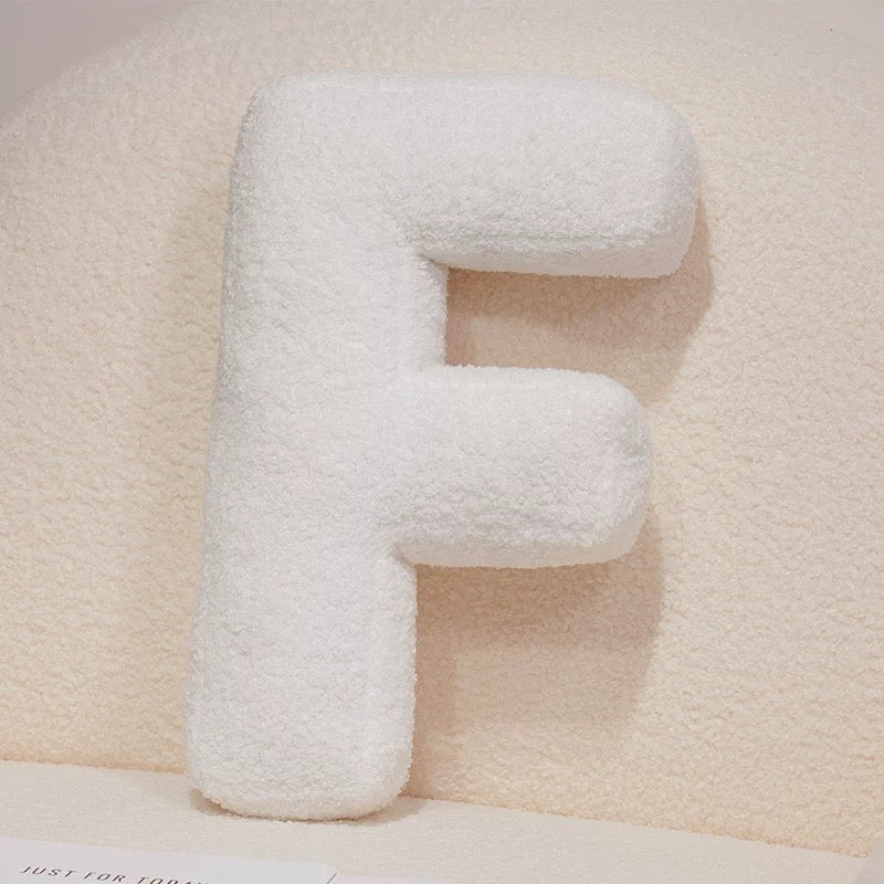 White letter 'E' pillow on a soft beige background