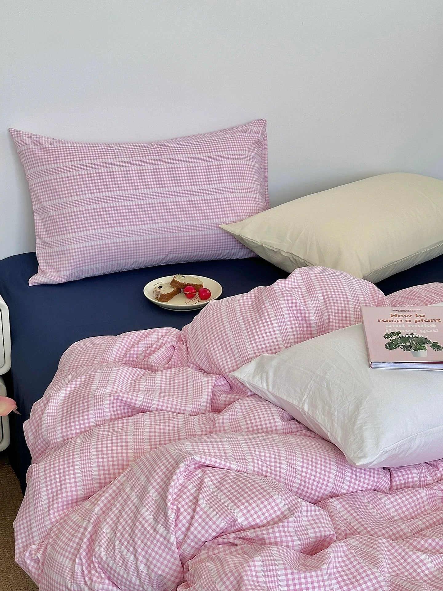 Bed with pink checkered bedding and pillows against a white wall.