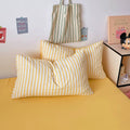 Yellow and white striped pillows on a bed with a striped bag and decorative items in the background.