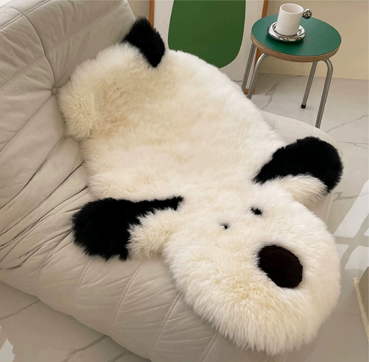 A cream dog rug drapes over a lounge chair, with black ears extending beside the face and rounded body.