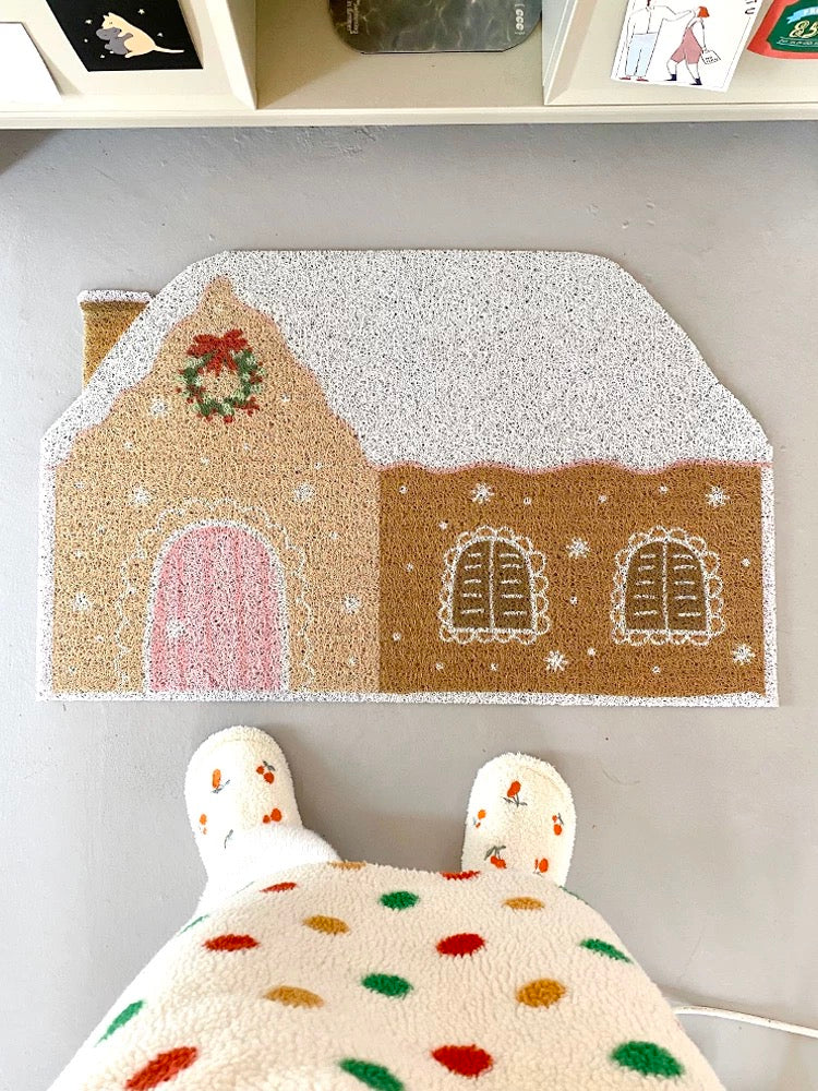 Cream gingerbread house doormat styled on wood flooring with white slippers