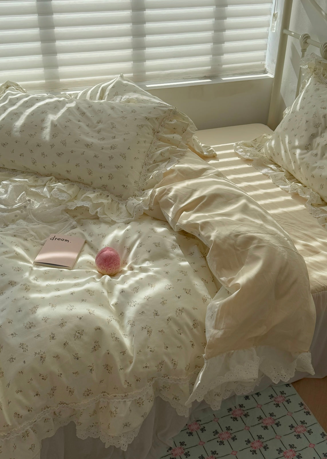 Delicate white lace bedding with a pink flower and book on a bed with white pillows.