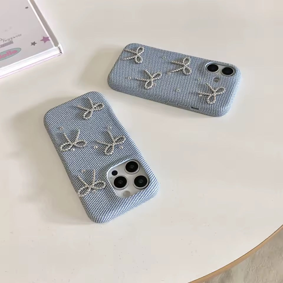 Two denim-style phone cases with bow designs on a white surface.