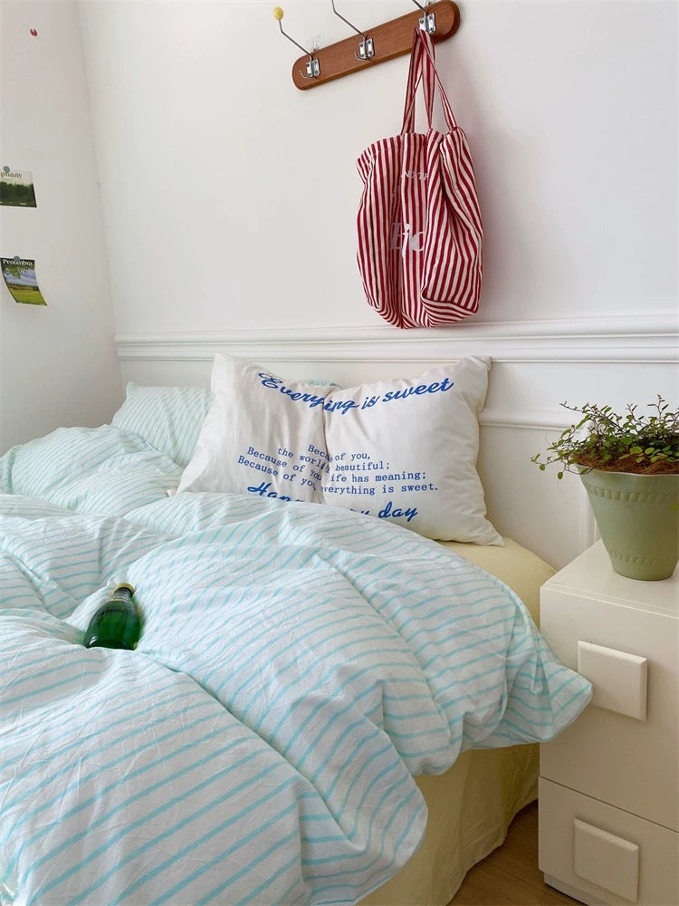 Bedroom with mint green bedding and a red and white striped bag hanging on the wall.