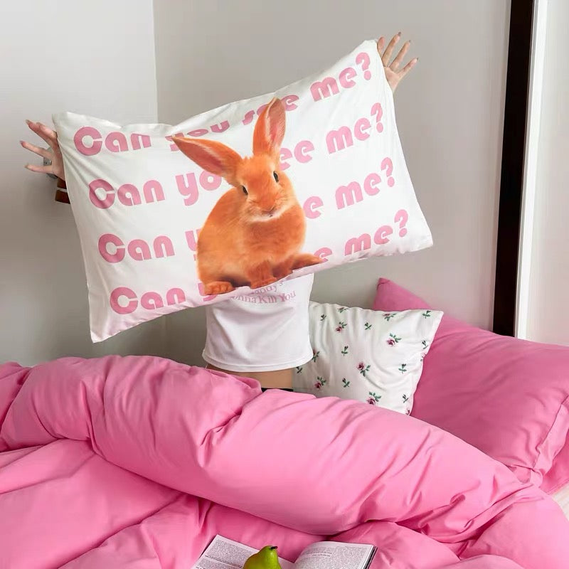 Person holding a pillow with a rabbit illustration and text 'Can you see me?' in a bedroom setting.