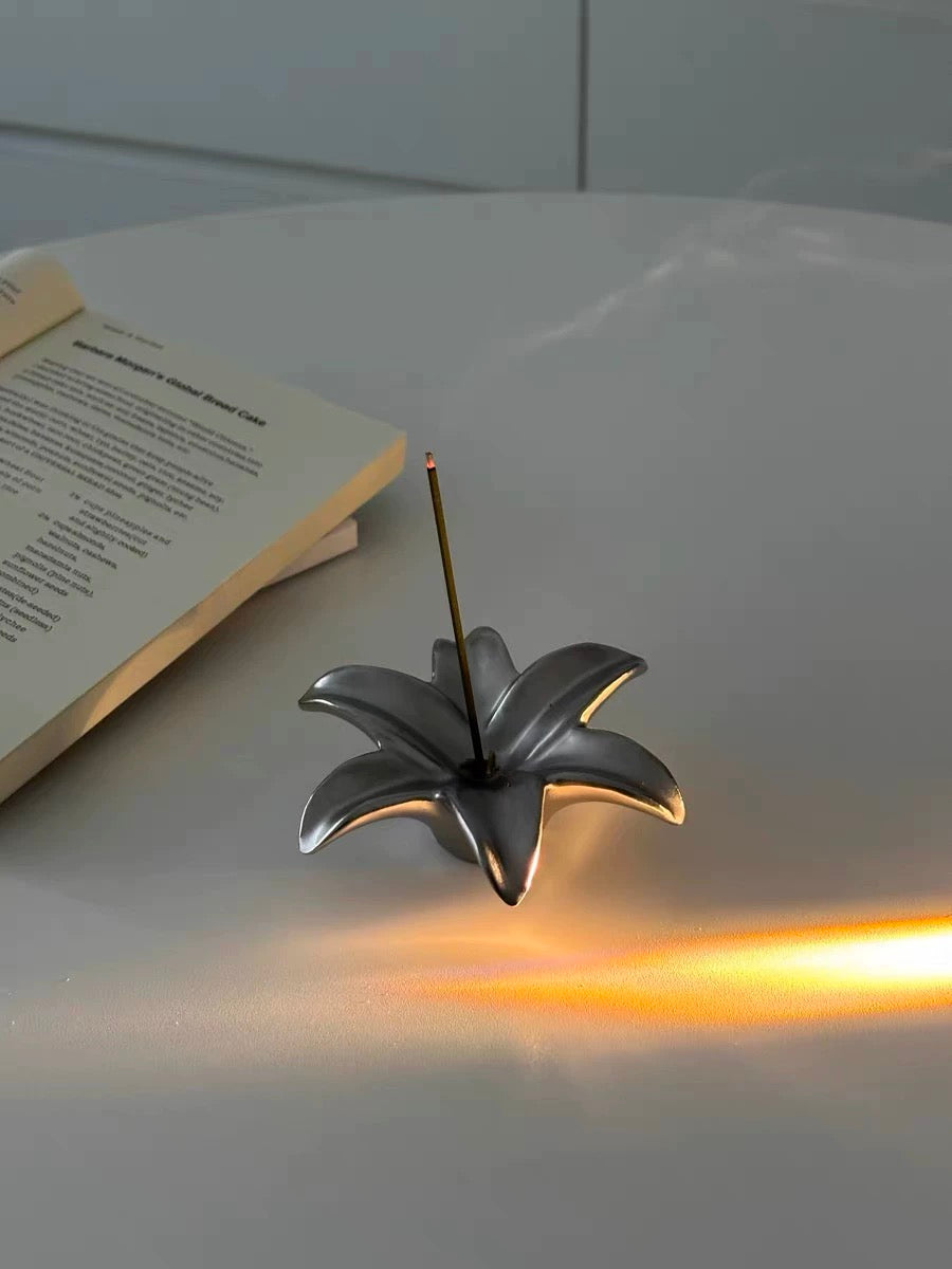 Decorative incense holder shaped like a flower on a white surface with an open book.