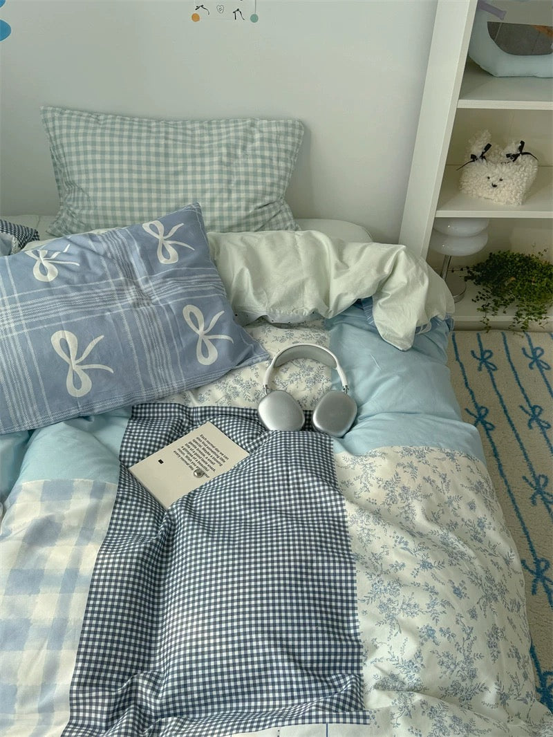 Bed with checkered pillow and blue bow-patterned blanket in a room setting.