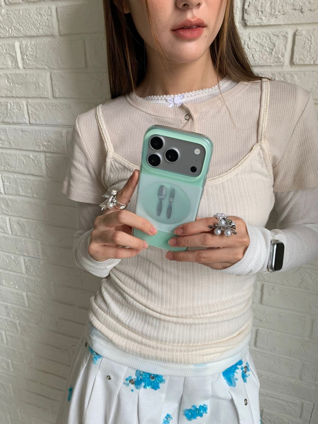 A mint green plate phone case in a wider mirror selfie, held sideways with its illustrated back visible.