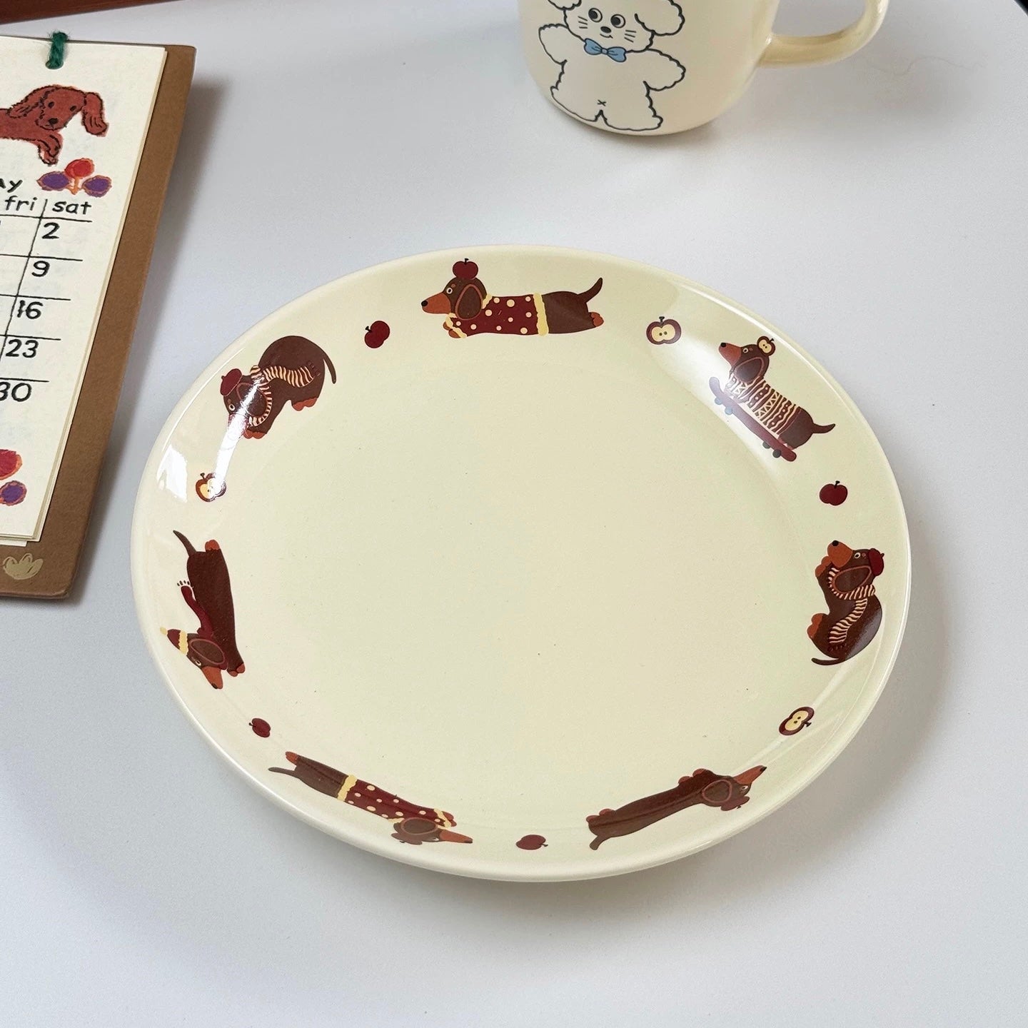 Cream ceramic dachshund plate on blue tabletop with wooden spoon resting across its center diagonally.