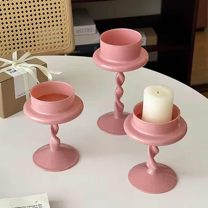 Set of three pink candle holders with candles on a white surface.