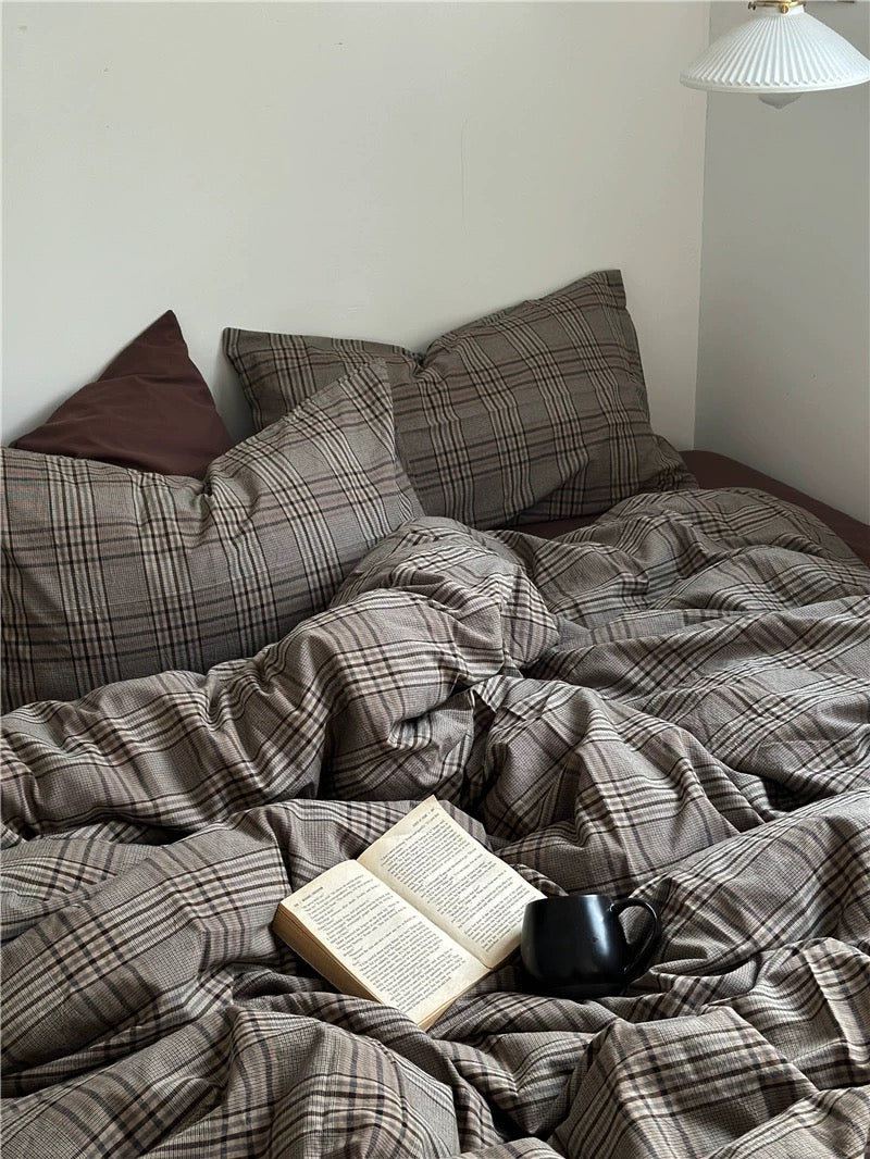 Bed with plaid bedding, pillows, and a book and mug on top