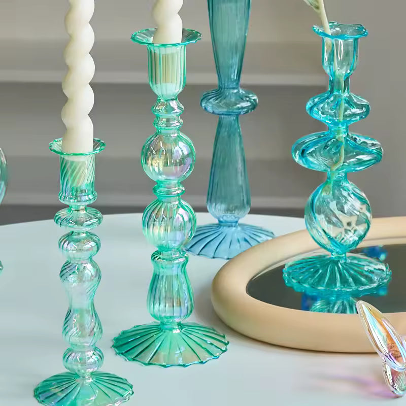 Turquoise glass candle holders with white candles on a reflective surface.