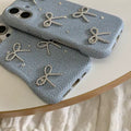 Two denim phone cases with silver bow designs on a white surface.