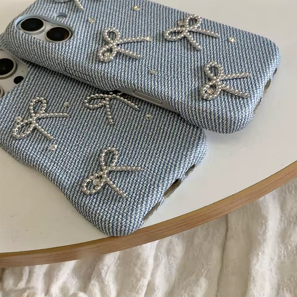 Two denim phone cases with silver bow designs on a white surface.