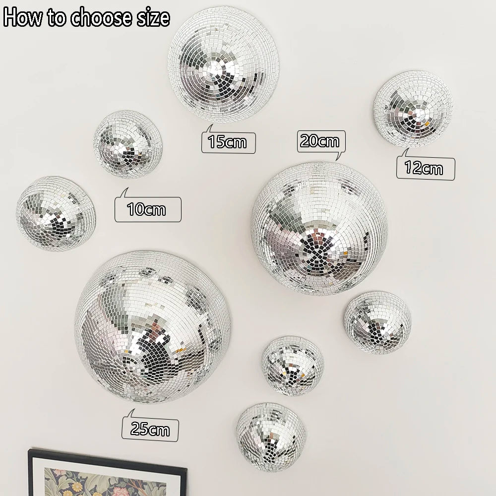 Set of silver disco balls of different sizes on a white wall.