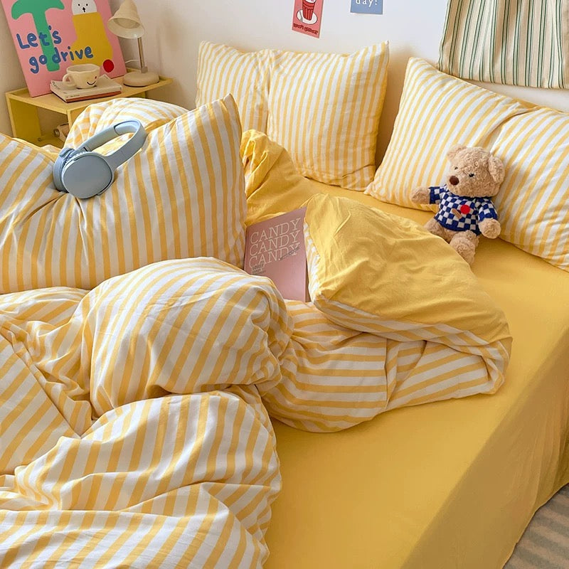 Yellow bedding set on a bed with decorative pillows and toys in a room.