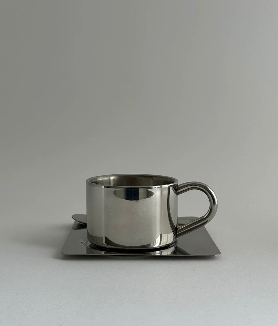 Stainless steel cup and saucer set on a light gray background