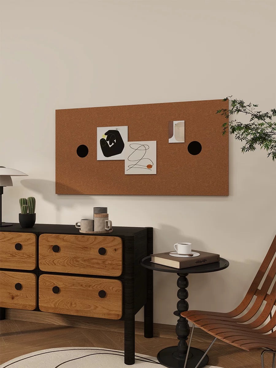 Bronze felt pin board with dark circular accents above a wooden cabinet beside a lounge chair.
