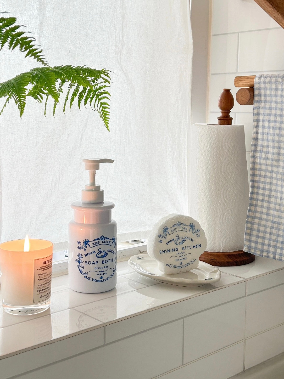 The floral soap dispenser stands beside a matching scalloped sponge, with blue swan artwork on white.