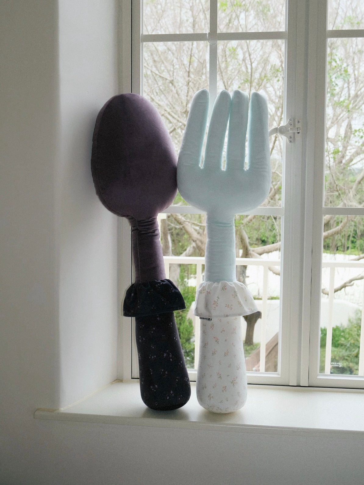 A purple spoon pillow stands beside a blue fork pillow, contrasting a dark handle with a pale floral handle.