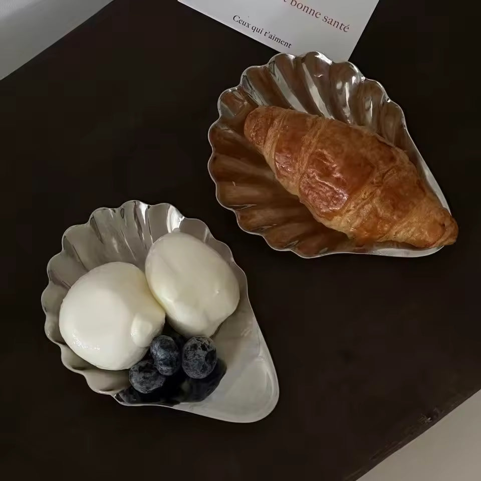 Two metal bowls containing a croissant, eggs, and berries on a dark surface.