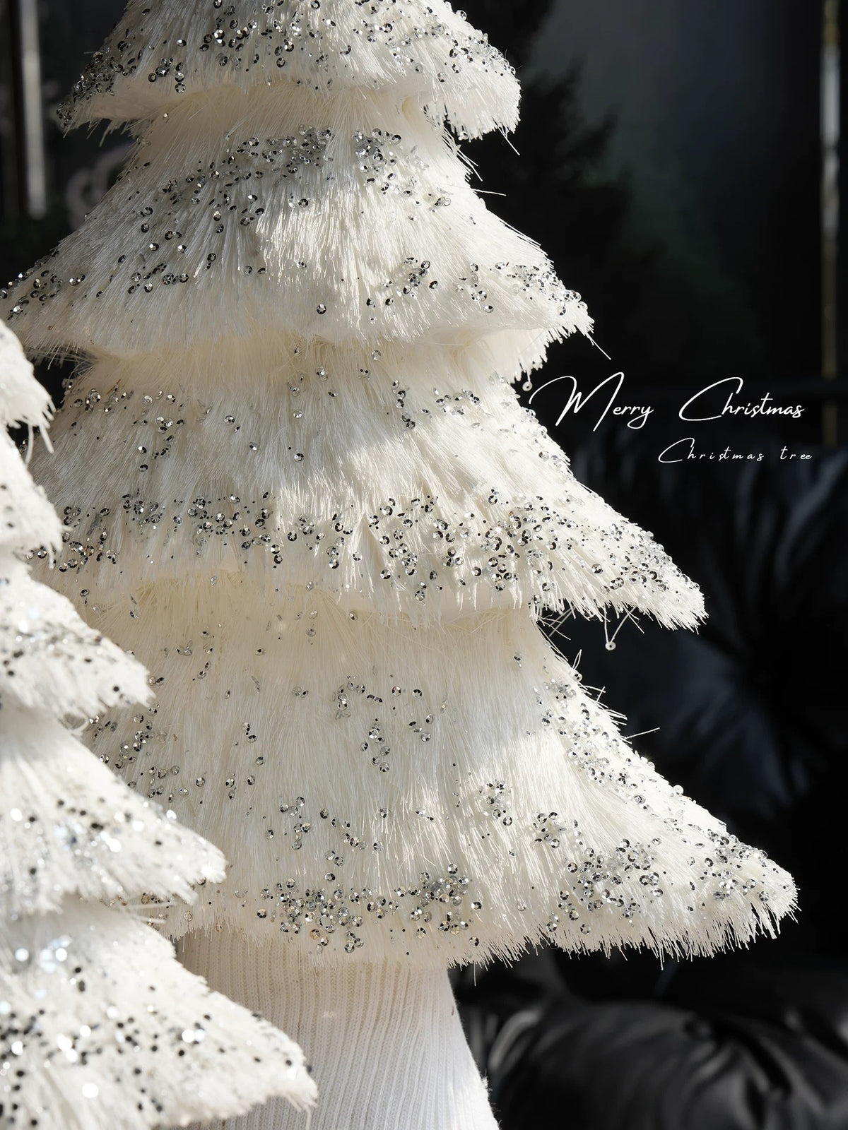 Fringed Christmas tree branches are shown close up, with shiny circular accents scattered among the white strands.