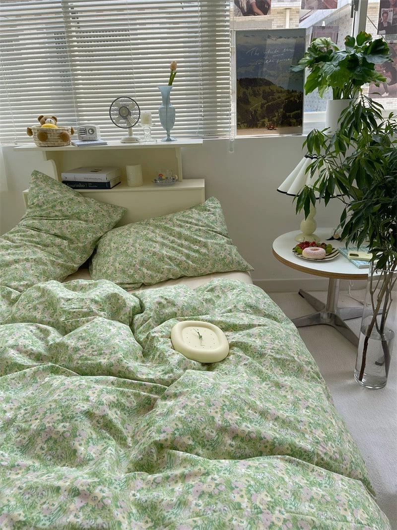 Bedroom with green floral bedding, a small table with a plant, and a window with blinds.