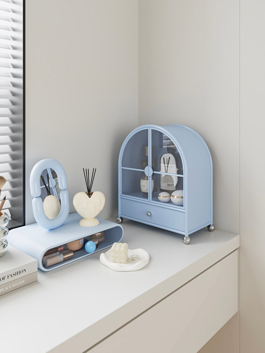 A blue perfume cabinet has arched glass doors, silver ball feet and a lower drawer beneath the bottles.