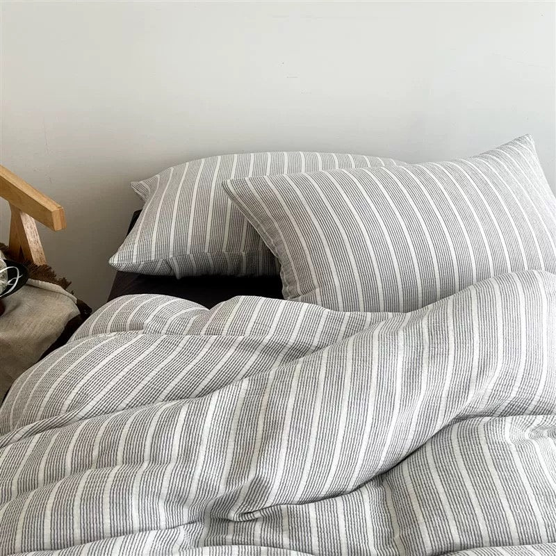 Gray and white striped bedding set with matching pillowcases on a bed, shown in a close-up interior shot.