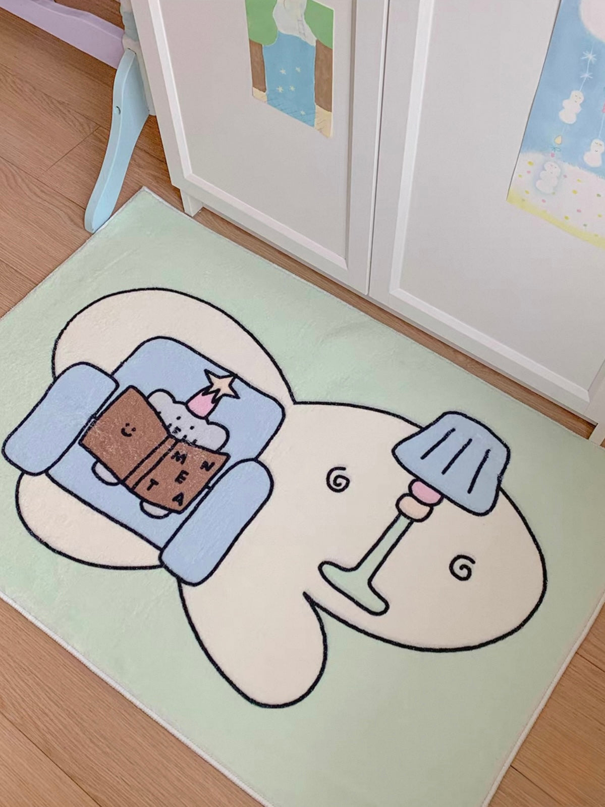 A green elephant rug lies beside a cabinet, showing the blue chair, open brown book and drawn floor lamp.