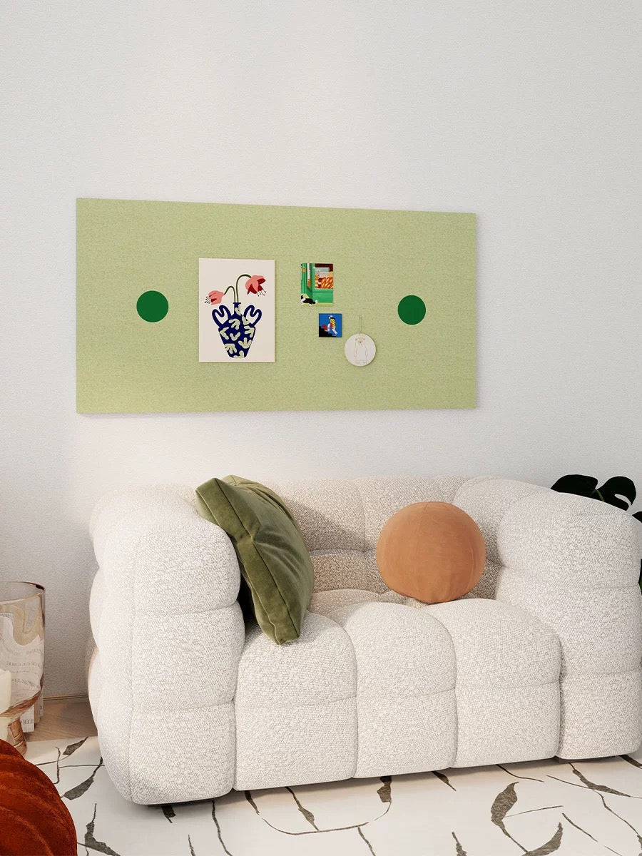 Green photo display board with pinned prints above a white sofa with green and orange cushions.