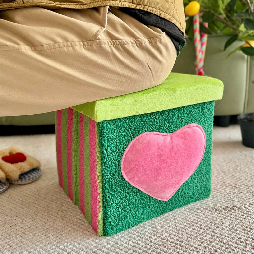 Green storage stool with pink heart styled beside a sofa