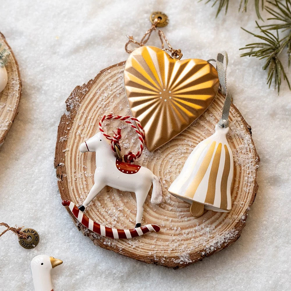 Hand painted Christmas ornaments show a gold heart, white horse with a red saddle and a striped bell.