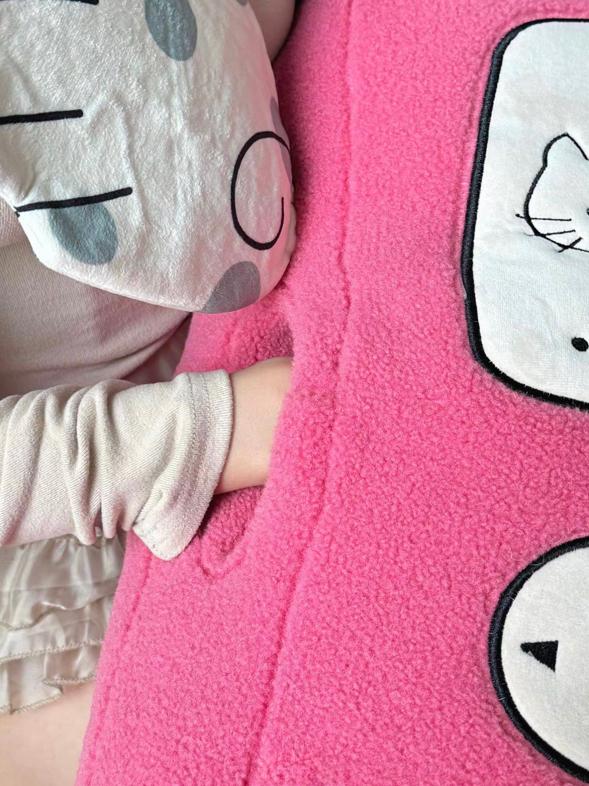 A hand slides into the side opening of a pink hand warmer pillow, beside the embroidered phone screen.