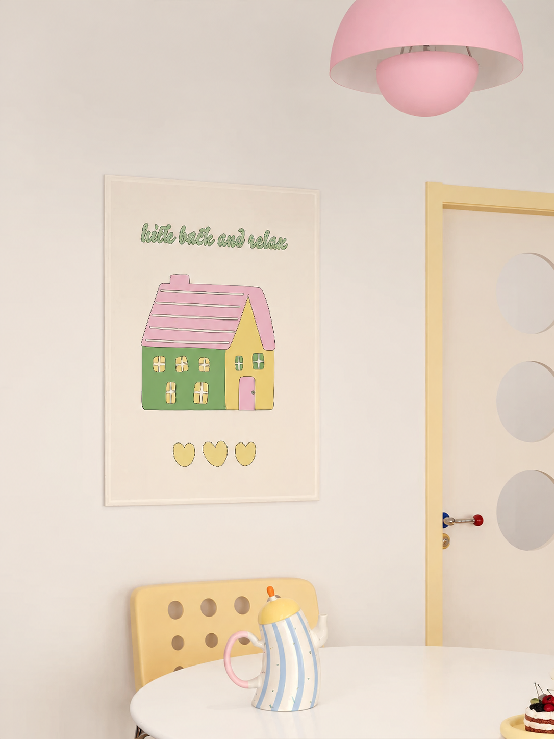 A house tapestry with a green house, pink roof and yellow hearts hangs above a small breakfast table.