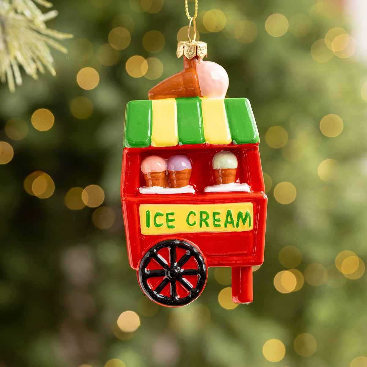 An ice cream cart ornament has a red body, black wheel and striped green awning beneath a pink cone.