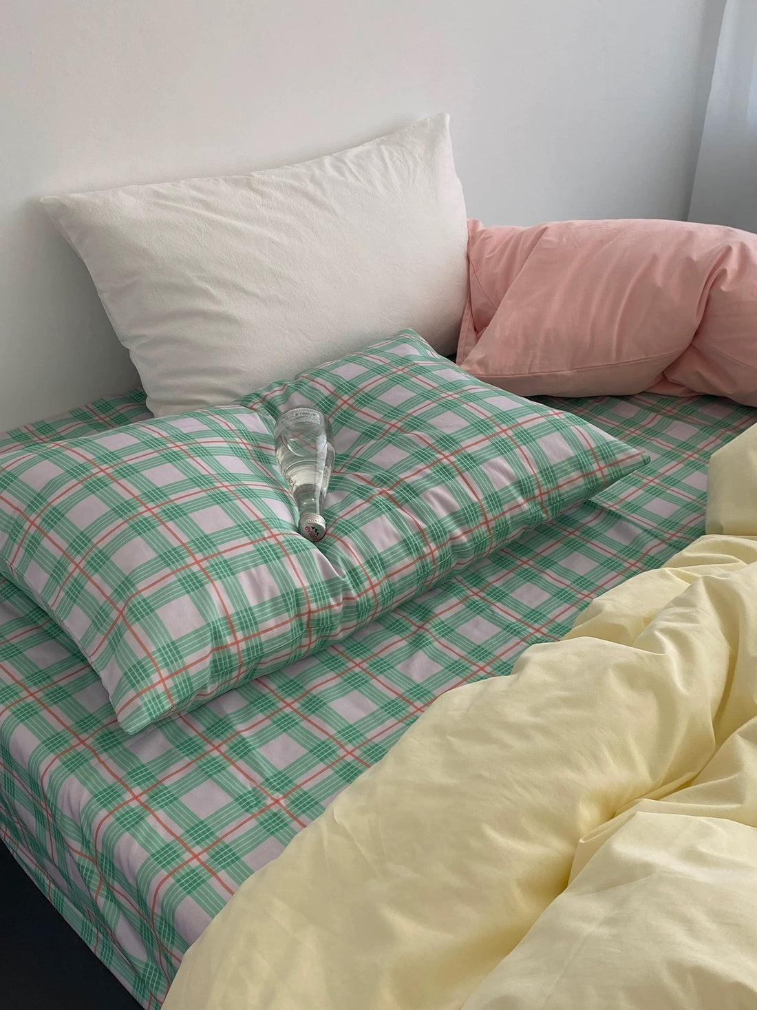 Bed with checkered green and pink sheets and pillows in various colors.