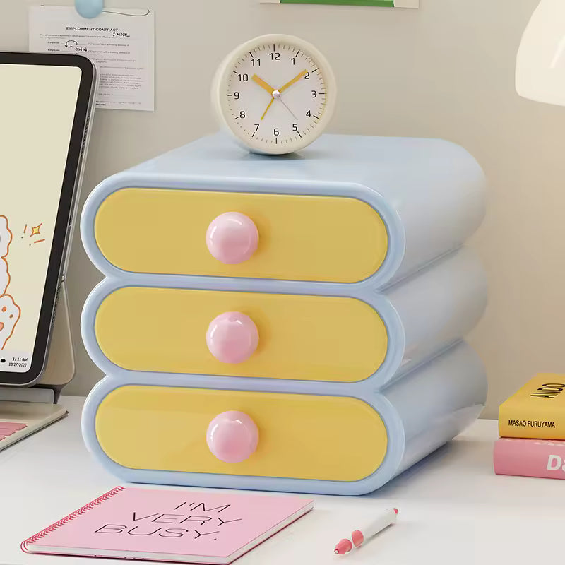 Pastel-colored three-drawer organizer with pink knobs on a desk, featuring a clock on top.