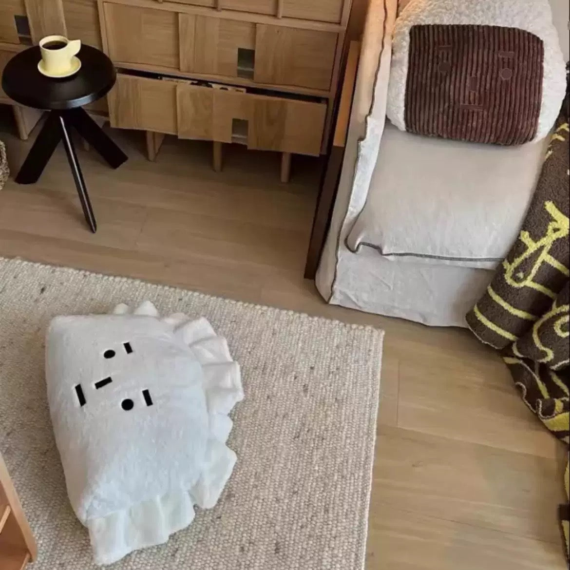 White cushion with black patterns on a textured rug in a room with wooden furniture and a chair.